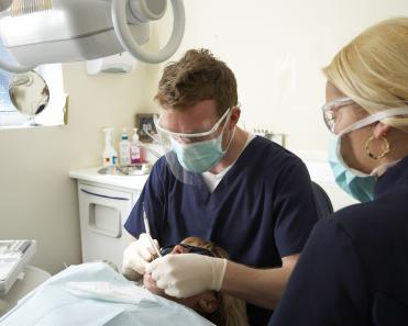 dental-male-and-female-colleague-treating-patient's-teeth