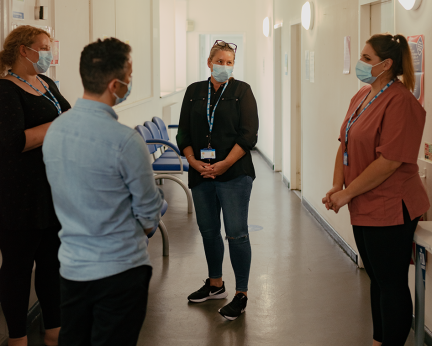 healthcare support worker in corridor wearing mask talking to colleagues