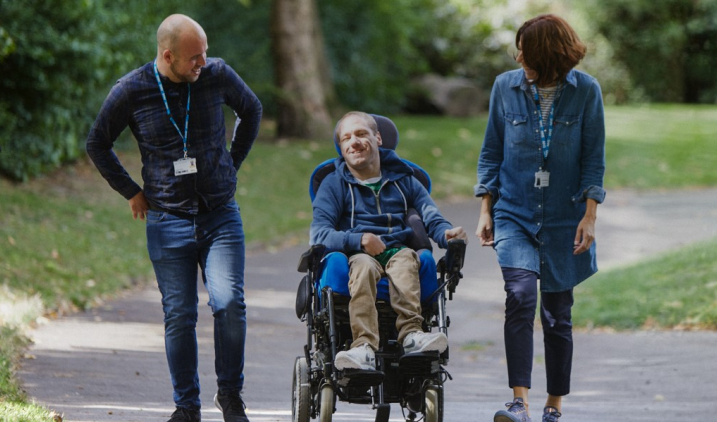 Two nurses talking to man in wheelchair