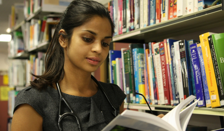 Female doctor reading book in library Female doctor reading book in library